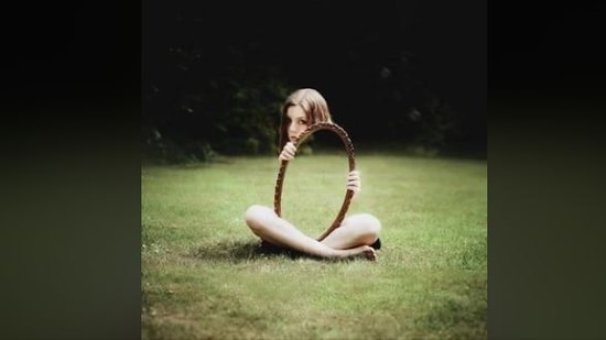 Optical illusions often go viral for how easily they trick our brains and eyes. But a recent post on Reddit has sparked a major debate, with users discussing whether the image is an optical illusion or the magic of some ‘clever editing'. The picture, shared by user @therealjustinjr on the Reddit page r/pics, shows a girl sitting on the grass while holding an oval mirror in front of her. At first glance, it looks like the mirror has turned invisible or is showing straight through her body. The grass in the background continues seamlessly inside the frame, creating the impression that her torso and legs have vanished.