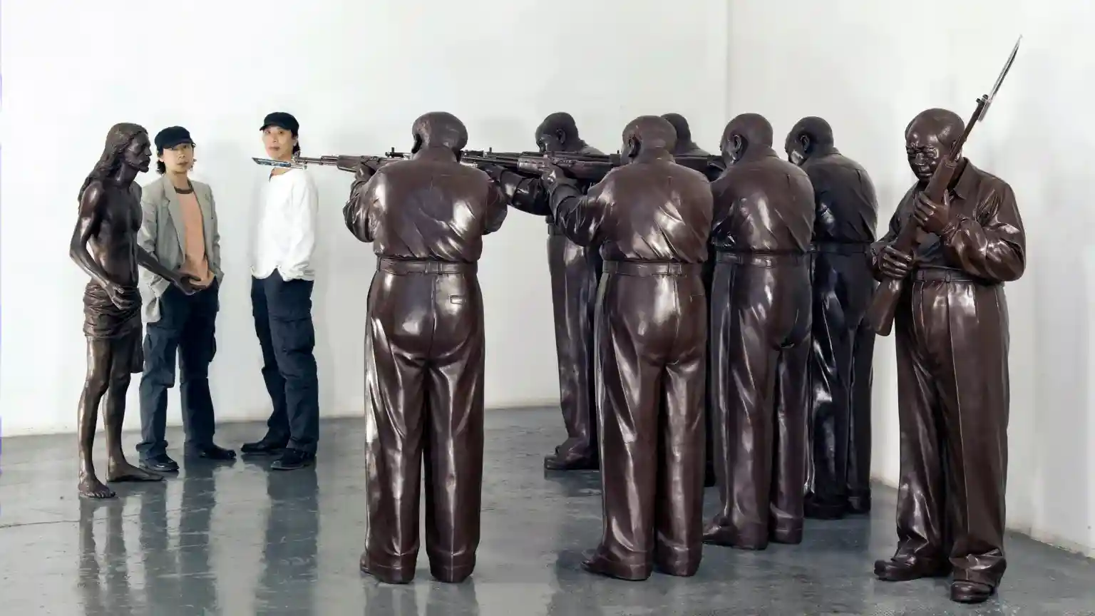 Jesus Christ stands at gunpoint, palms upturned, seven figures in a firing squad around him. The bronze riflemen are unmistakable in their likeness