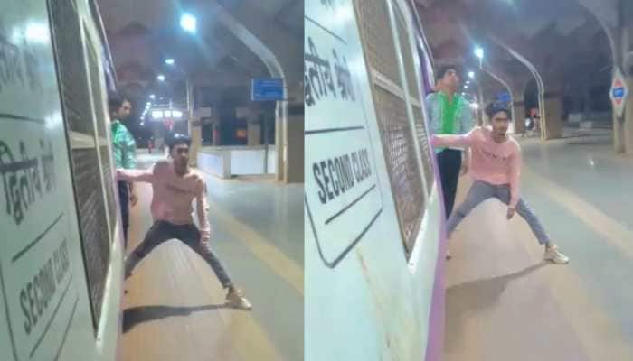 In a reckless stunt caught on camera, a teenager was seen hanging from a moving Mumbai local train and even trying to snatch a commuter's phone. Social media is flooded with unusual reels, but the problem begins when people put their lives at risk for a few likes. Dangerous stunts may cost lives, yet some seem to value attention over safety. A recent video, reportedly from a Mumbai local train, shows a boy, identified as Rahul Kumar Yadav, hanging dangerously with one foot inside the train and the other dragging along the platform, while a friend films him from the front gate.