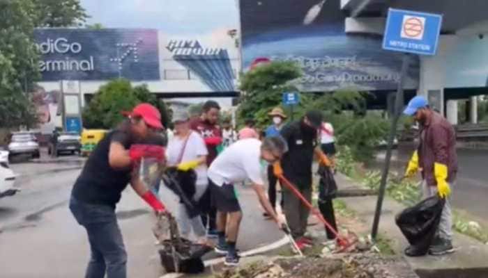 Local residents and foreigners participated in the gurugram cleanliness drive on Sunday, raising questions on municipal bodies and civic authorities. A citizen-led cleanliness drive in Gurugram on Sunday has sparked widespread discussion on social media, with residents expressing frustration at authorities and the municipal administration. <br> <br> The initiative was led by both local residents and foreign nationals living in Gurugram, aimed to clear roads, drains, and public spaces across the city.<br> <br> The drive began near the Guru Dronacharya Metro Station and drew attention for its rare display of civic unity. Participants focused on collecting litter, unclogging drains, and spreading awareness about cleanliness in the bustling Millennium City.<br> <br> While many praised the effort, several netizens expressed their disappointment with the authorities, questioning why citizens had to take matters into their own hands.